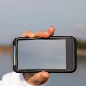 Hand showing smart mobile phone with blank screen, beach background