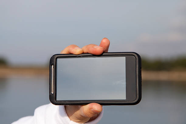 Hand showing smart mobile phone with blank screen, beach background
