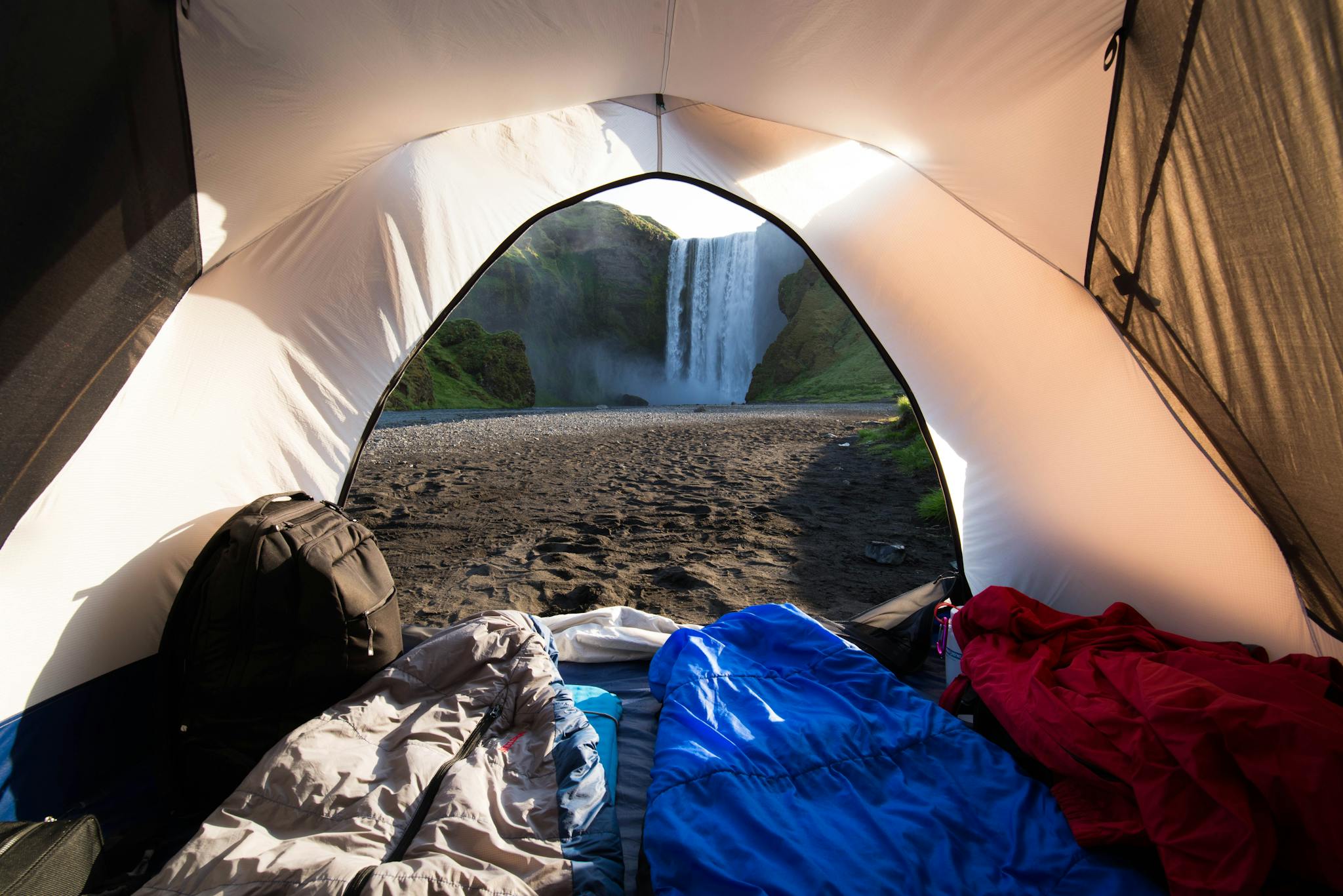 View from a camping tent interior looking at a scenic waterfall in a wilderness setting.